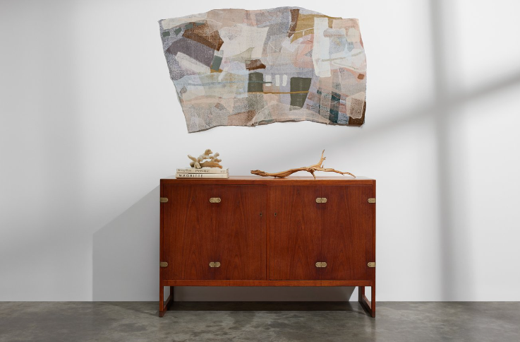 Image contains a wall art made out of pre-worn clothes under Eileen Fisher's flagship Waste No More. It is hanging above a wooden closet.