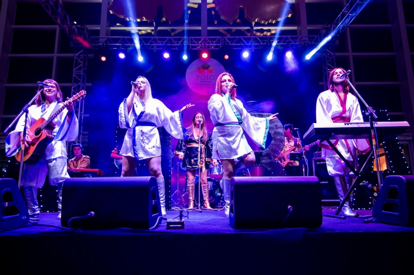 Pessoas no palco iluminado tocando instrumentos e cantando

Descrição gerada automaticamente