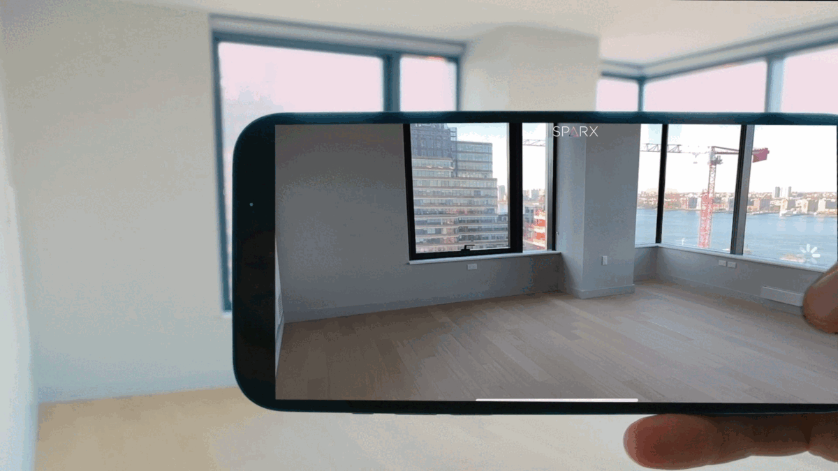 An iPhone held gracefully in a hand, showcasing the SparX app in action on its screen. Witness the seamless transition of furniture appearing and disappearing, demonstrating the app's innovative features