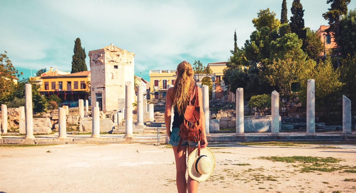 A person standing in a dirt area with a hat and a building behind her

Description automatically generated