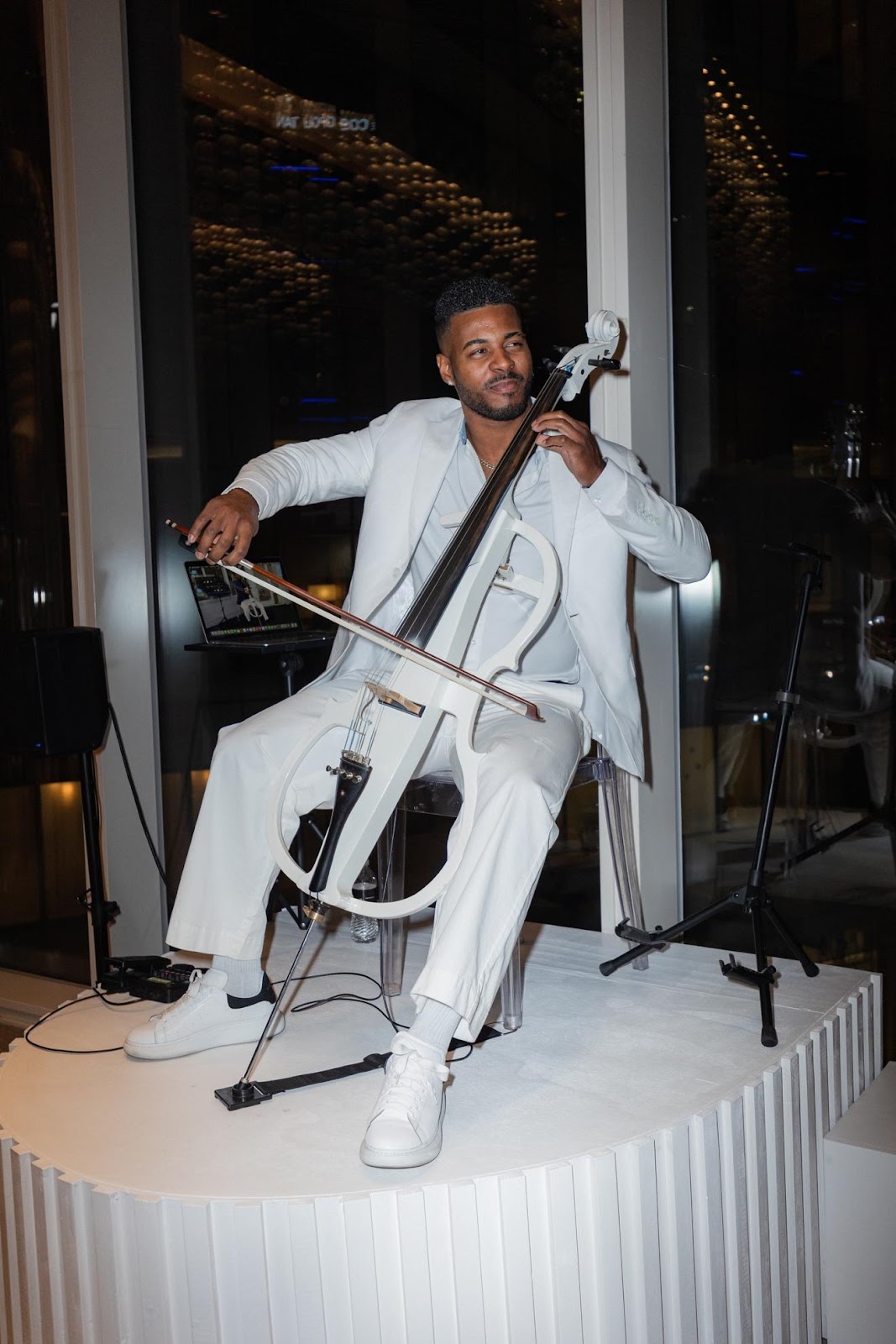 A person in white suit playing a cello

Description automatically generated