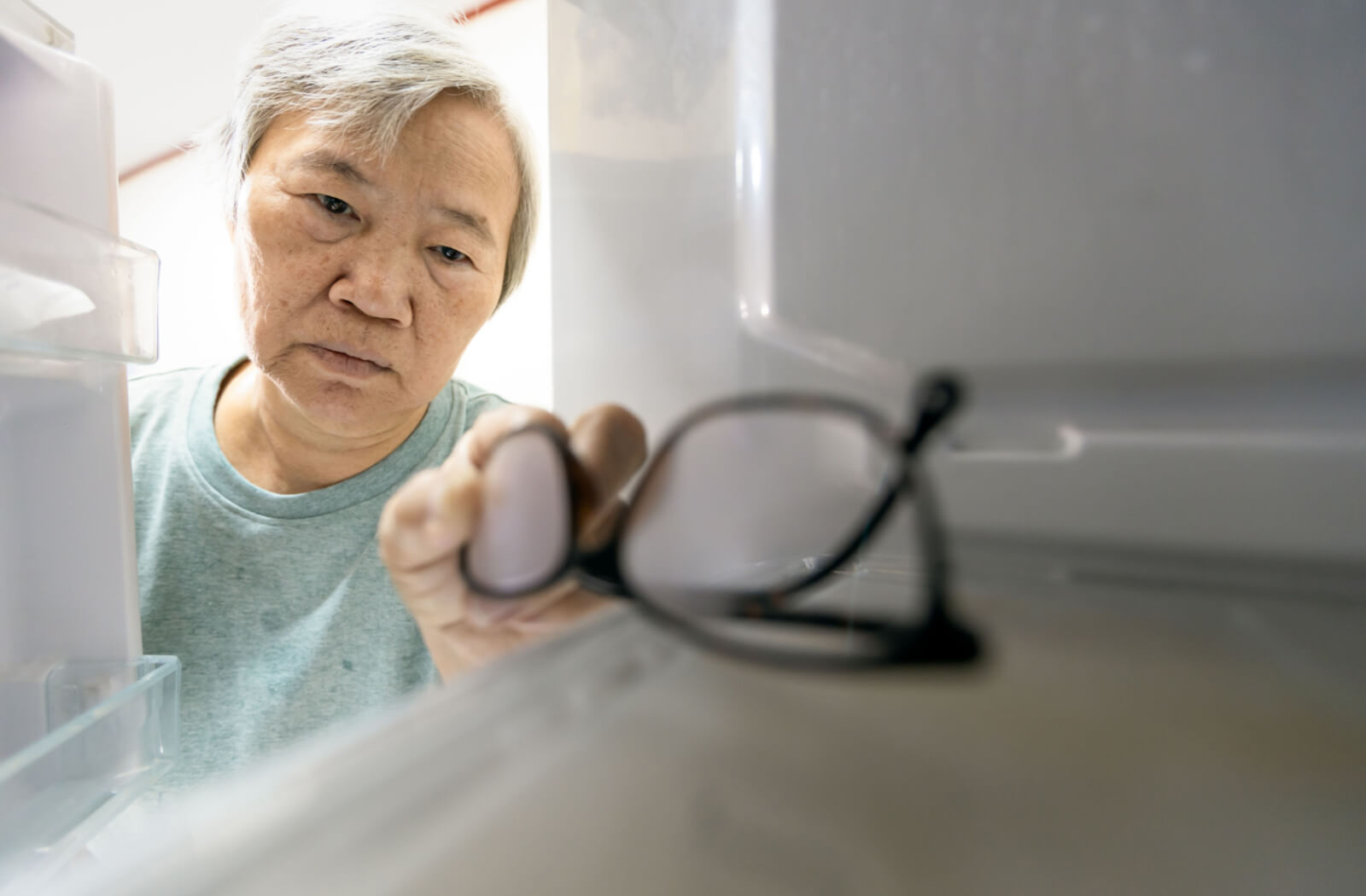 A senior woman with memory impairment symptoms storing her glasses in the fridge.