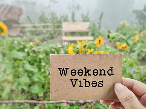 Weekend Vibes Written on Brown Card & It's Picked in a Hand With a Picturesque Greenery in the Background