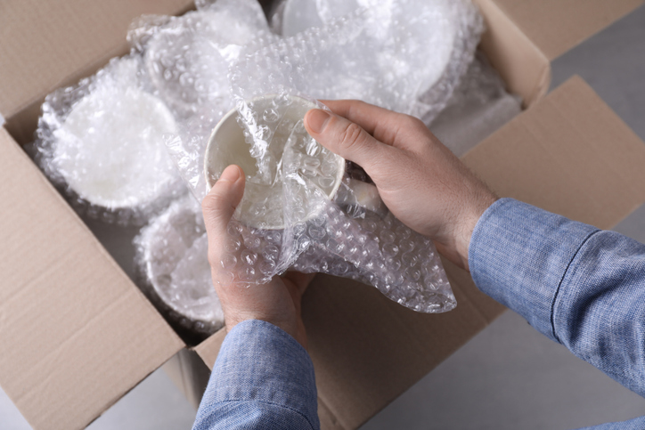 Man covering ceramic dishware with Bubble Wrap.