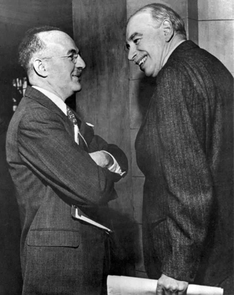 John Maynard Keynes stands with Harry Dexter White, another prominent economist. They are both wearing dark suits and White has his arms crossed. They are smiling. 