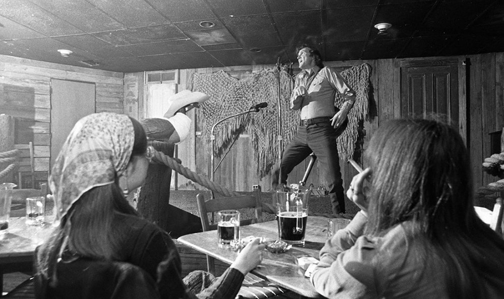 Old image of a live performer at Village District while patrons drink and smoke