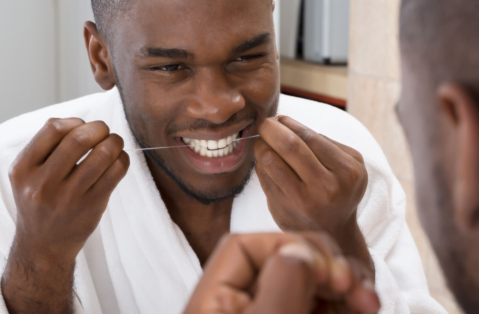 A man in a white robe cleaning his teeth using a dental floss.