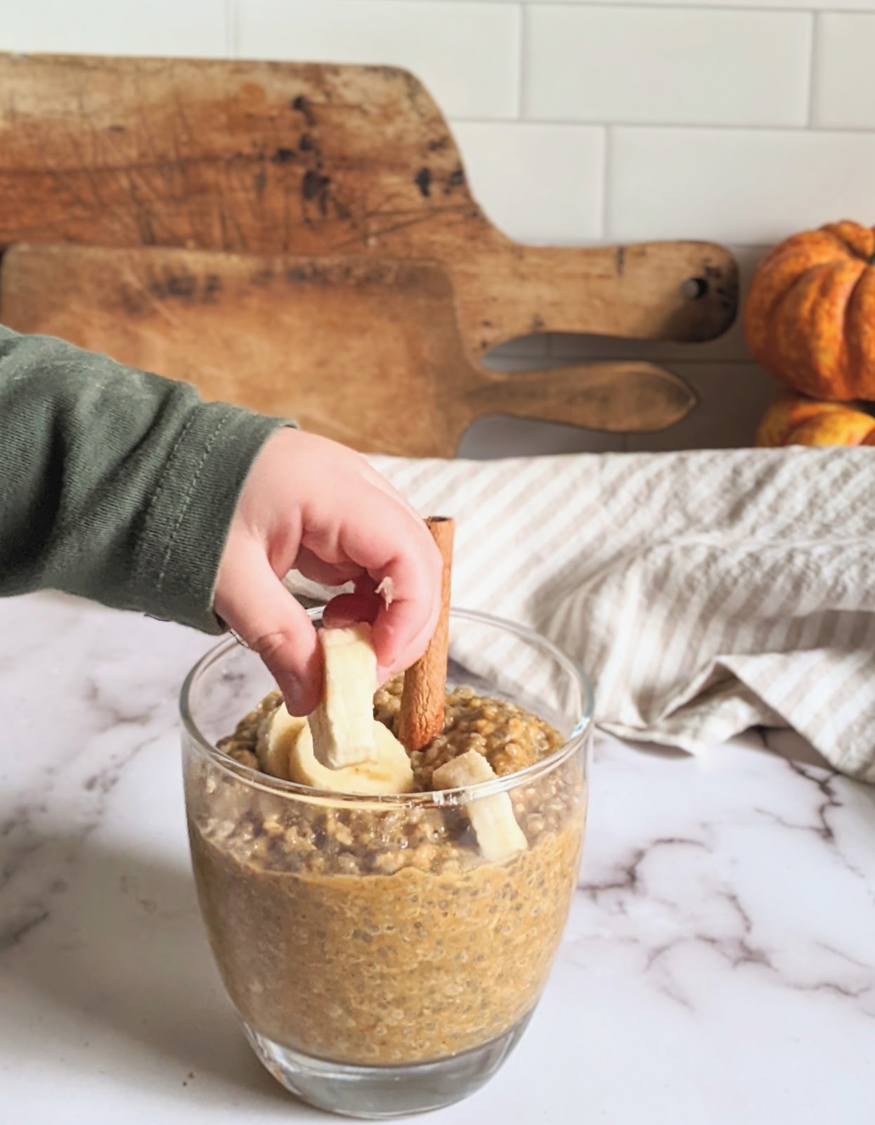 close up of a child's hand reaching for a banana slice in a jar of pumpkin pie chia pudding
