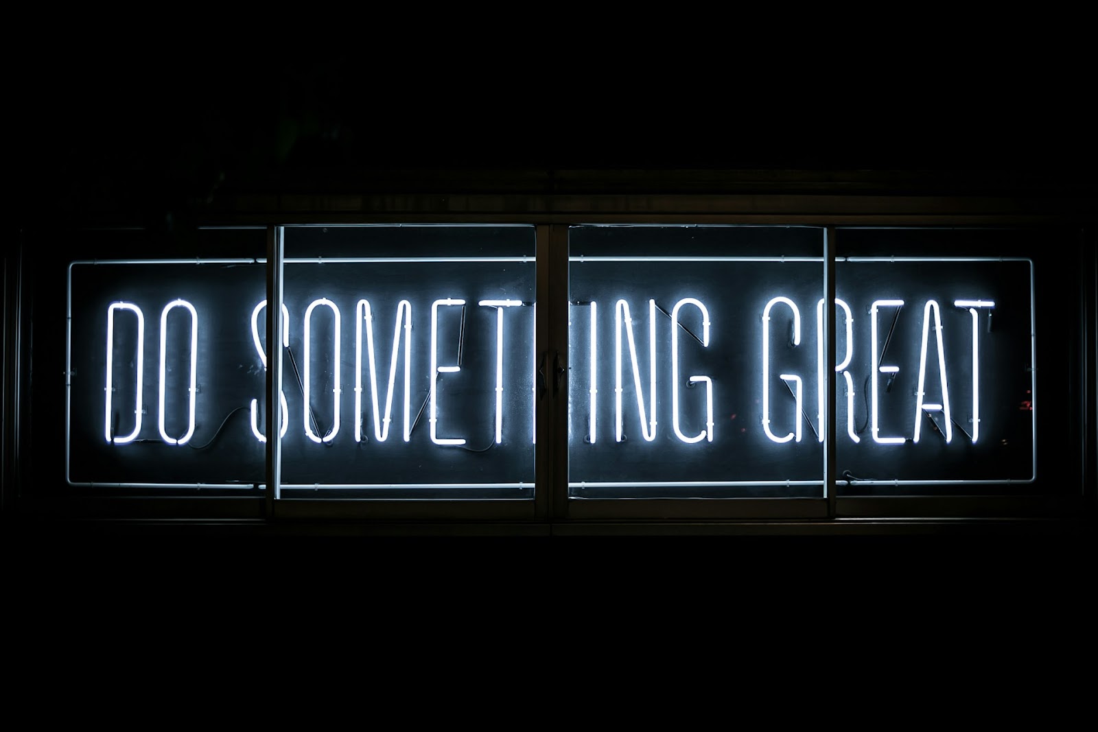 A neon sign in a window with the word 'Do Something Great'