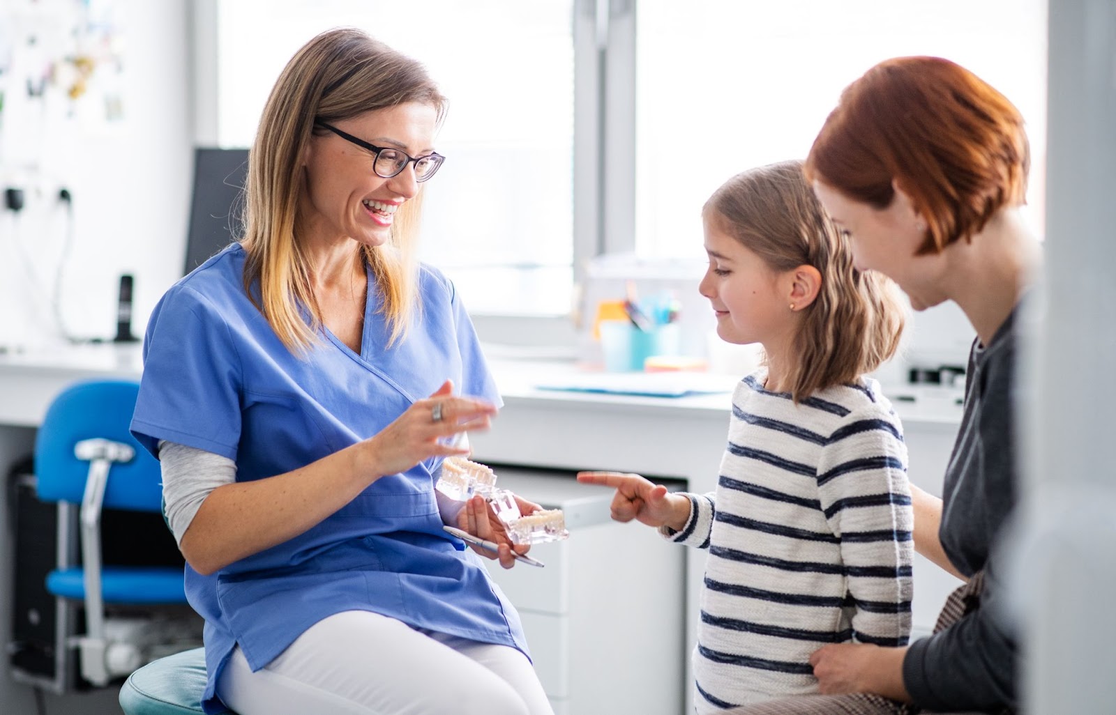 dentist showing young patient the teeth structure with her mom in the dental clinic 