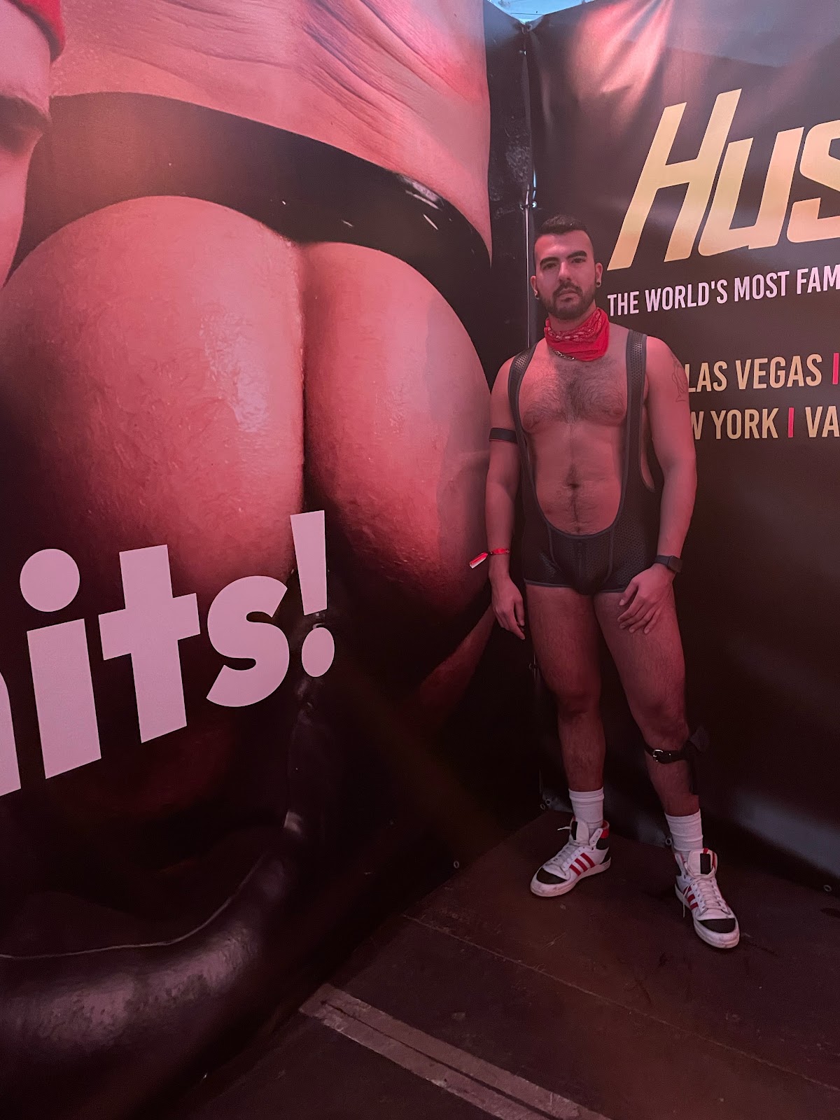 gay onlyfans content creator phil wearing black leather fetish gear standing in front of a bare ass billboard at darklands 2024
