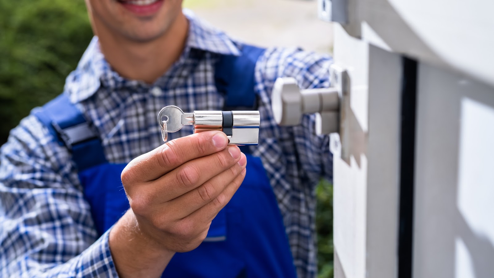 A commercial locksmith holds a cylinder lock and key, ready for a lock rekey service at an outdoor gate.