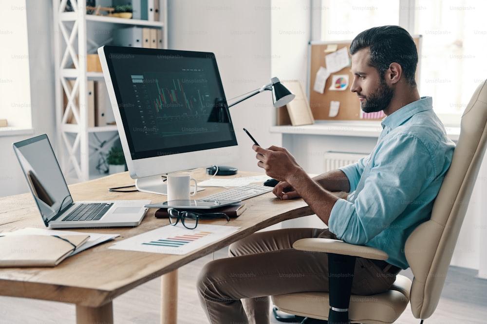 Young modern businessman using smart phone while sitting in the office