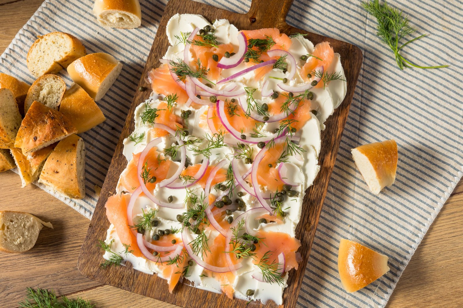 A close-up photo of a wooden cutting board topped with cream cheese, lox, onion, capers and dill. This bagel and lox bliss board is one of many great Breakfast and Brunch Board Presentation Ideas.