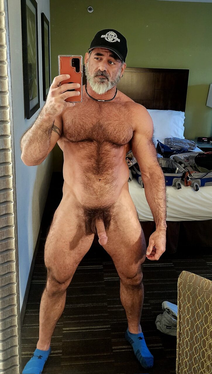Lawson James posing naked taking an android mirror selfie in front of a bed with empty open luggage 