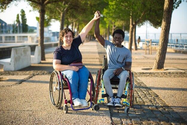 Portrait of biracial family on romantic date in park. African American man and Caucasian woman in wheelchairs, holding hands, smiling. Love, relationship, happiness concept