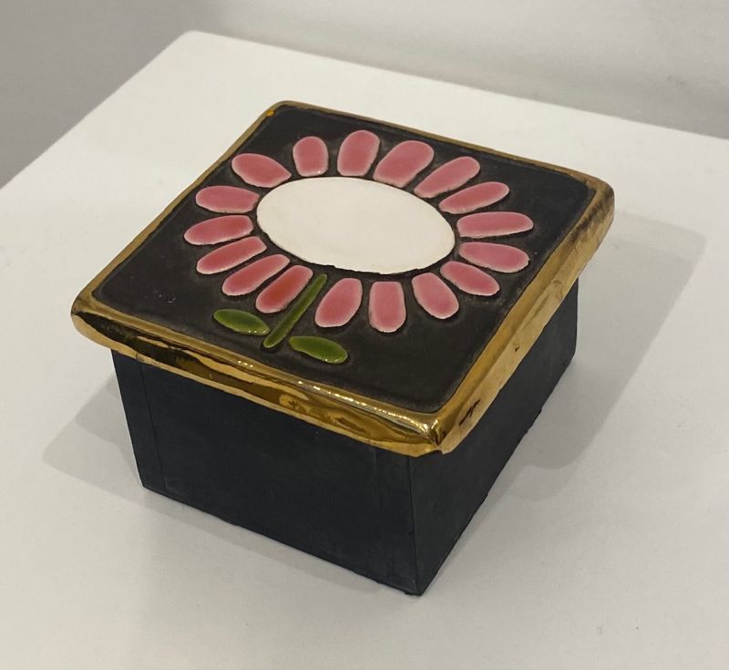 Una caja de joyas de madera de Mithé Espelt. La tapa de cerámica está dorada con hoja de oro y adornada con una flor esmaltada.