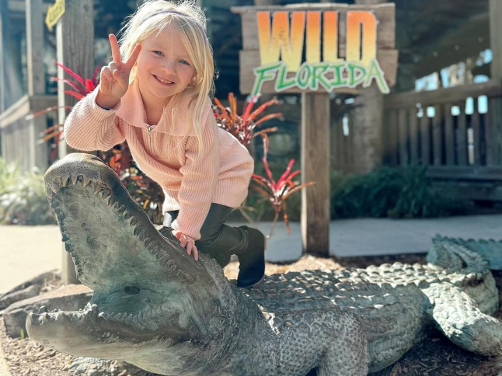 A young girl poses on top of a gator sculpture at Wild Florida's Gator Park