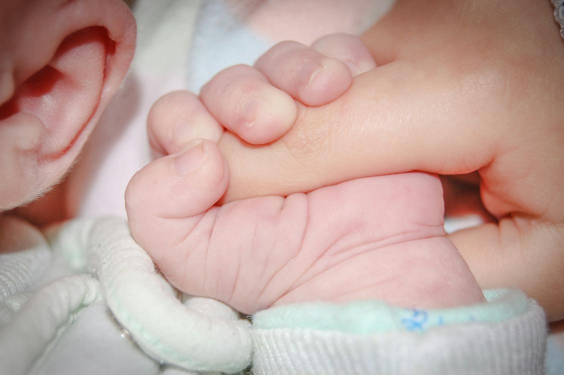 Free Touching moment of crop anonymous newborn infant with tiny hand lying on soft bed and gently grasping parents finger Stock Photo