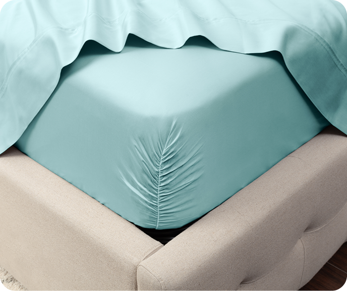 Our light aqua blue Eucalyptus Luxe Sheet Set in Shoreline shown on a mattress with flat sheet pulled back to display the fitted sheet.