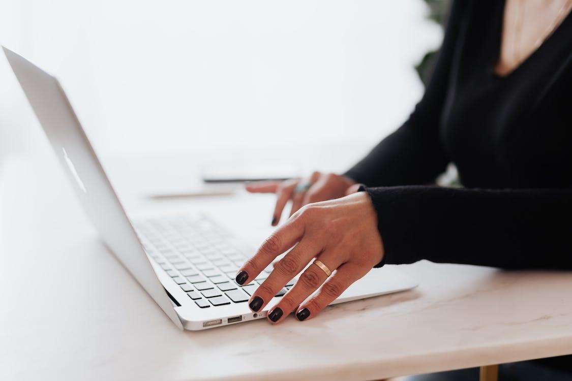 Free Crop unrecognizable female entrepreneur in casual clothes using touchpad on laptop while working at table in contemporary office Stock Photo