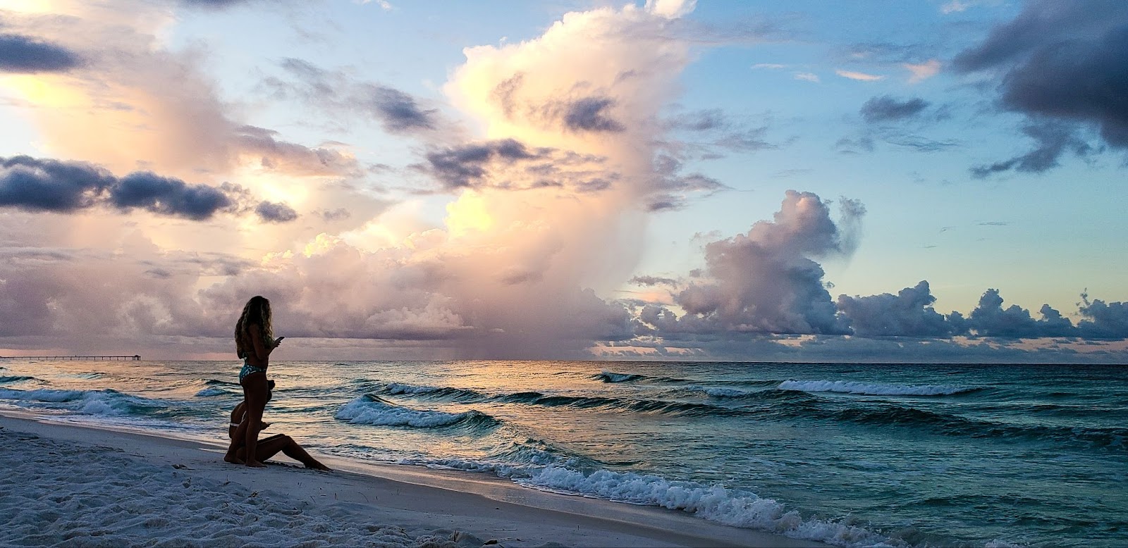 Two girls stand on the sandy beach, immersed in the beauty of the early morning sky during the golden hour. 