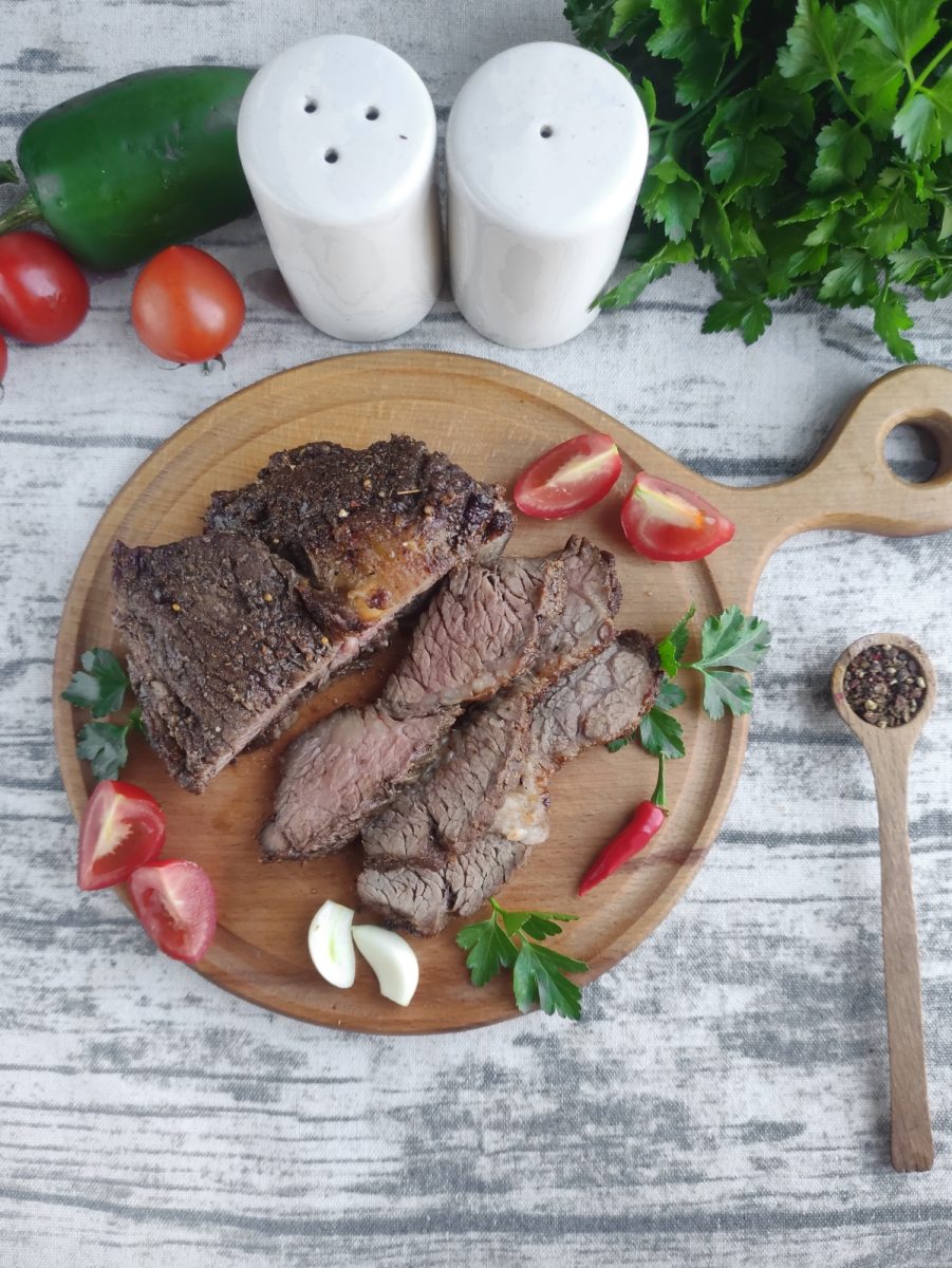Ribeye steak on a wooden cutting board with tomatoes and peppers, cooked to perfection in an air fryer.