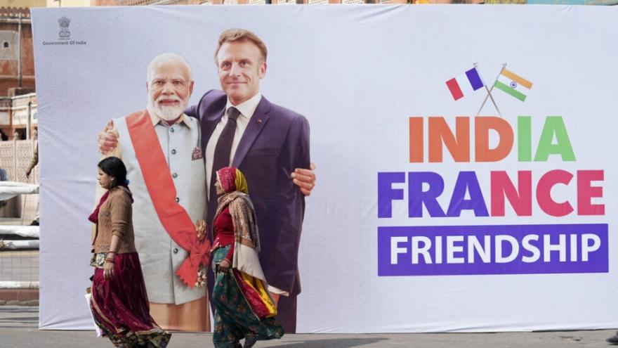 Two Indian women walk past a billboard showing French President Emmanuel Macron with Indian Prime Minister Narendra Modi erected ahead of Macron's arrival in Jaipur, Rajasthan, India, Thursday, Jan.25