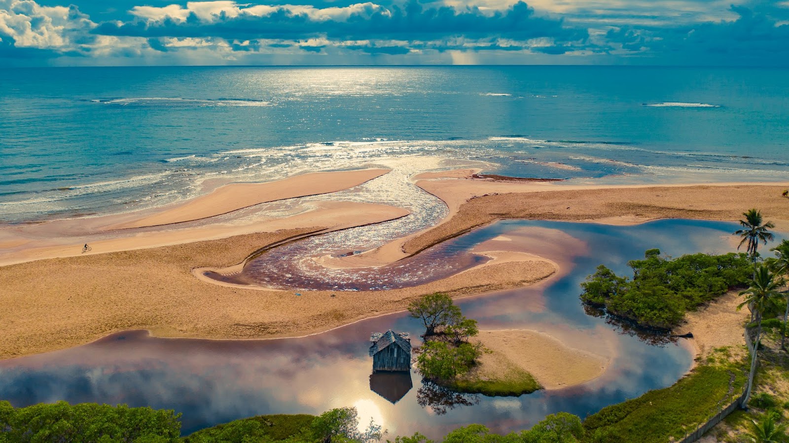 Vista aérea da Praia dos Nativos. Mar azul ao fundo da imagem vindo de encontro à faixa de areia, onde se mistura com o Rio Trancoso, que vai até a parte inferior da imagem.