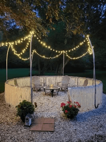 An old trampoline frame turned into a hangout spot with chairs and lights.