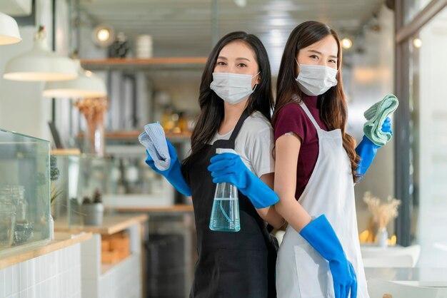 Free photo portrait of asian waitress with apron staff wearing protection rubber glove face mask protection hand hold cleaning towel and alcohol spray disinfectant for protect infection coronavirus health ideas