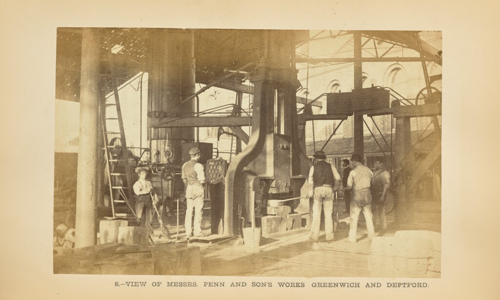 Black and white photo of men, most with their backs turned, working in some kind of factory