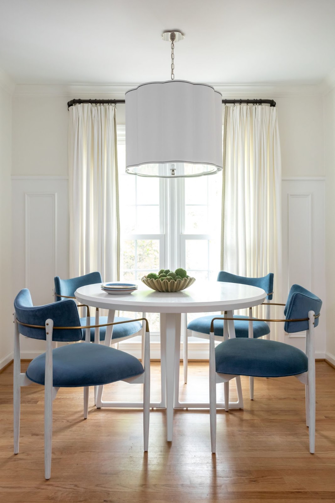 Blue chairs around white dining table. Lamp shade chandelier hangs above. 