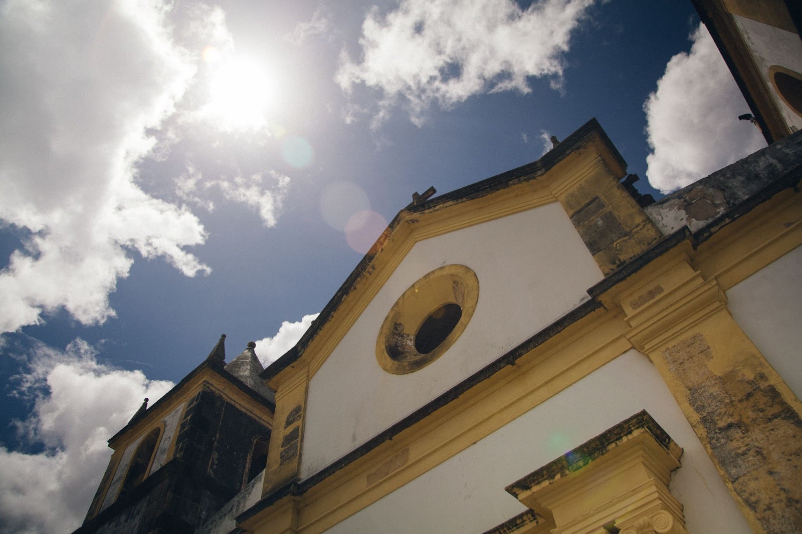 Foto de uma das igrejas de Jaboatão dos Guararapes vista de baixo para cima. Detalhes arquitetônicos antigos, com céu azul e nuvens brancas