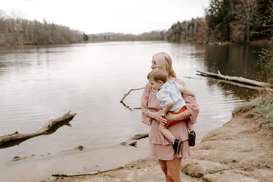 A person holding a baby by a body of waterDescription automatically generated