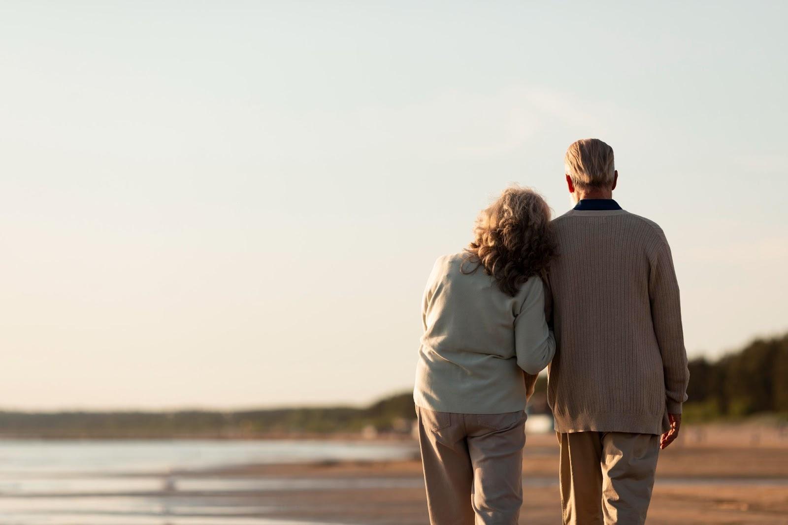 An elderly couple holding hands on a beach

Description automatically generated