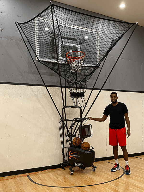A basketball player standing besides a shooting machine during training