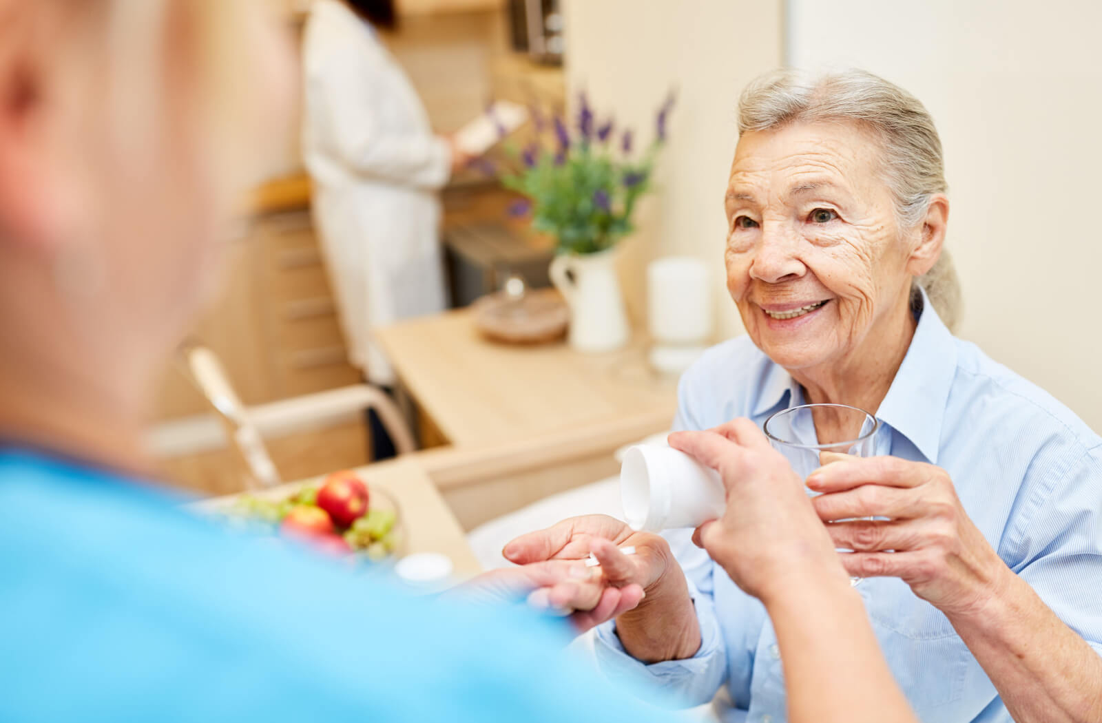 An older adult woman receiving her medicine from an assisted living staff.