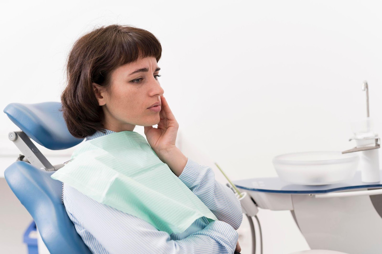 Женщина в кресле стоматолога держится за щеку