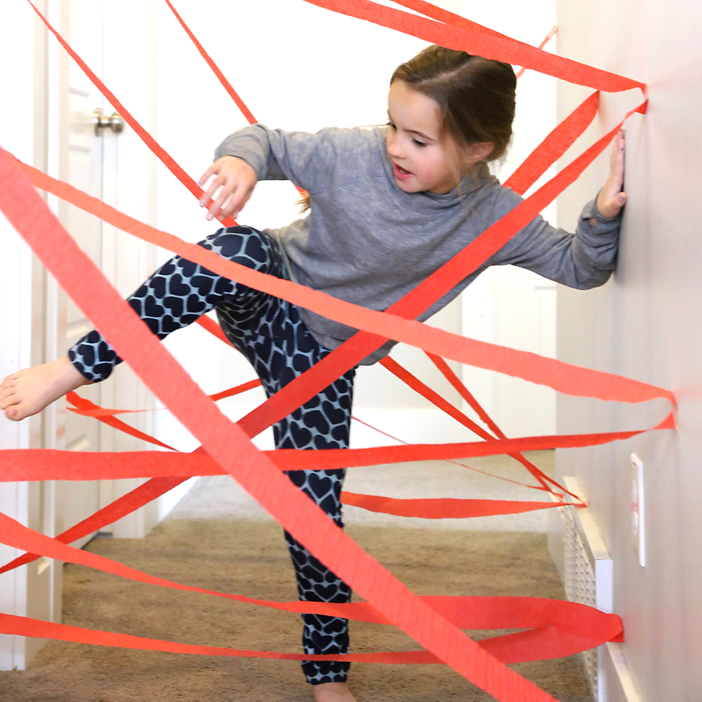 Girl crawling through maze made from crepe paper in a hallway