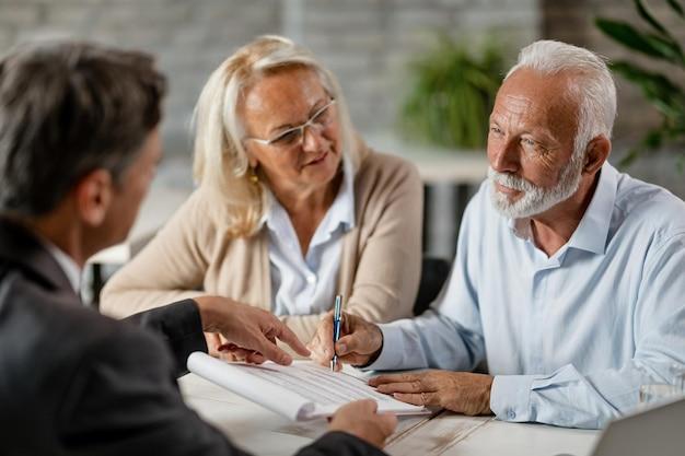 Mature couple having a meeting with bank manager and signing lease agreement in the office focus is mature man