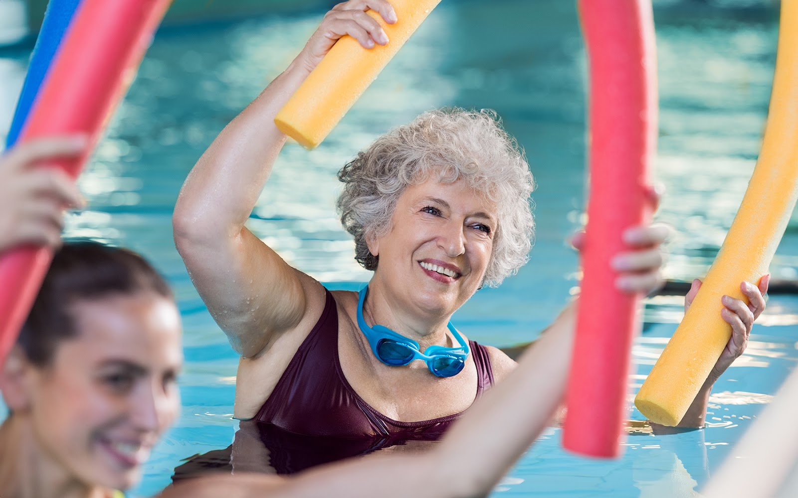 instructor and older women using pool noodles in water aerobics class