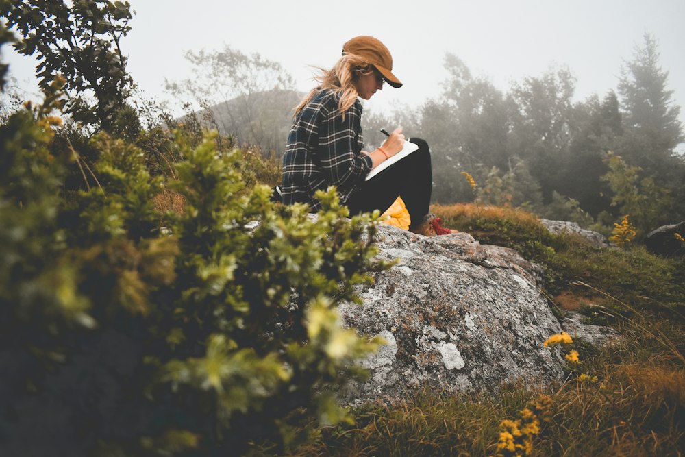 A women sitting on a rock outside writing in a journal - Writing Prompts to Relieve Stress & Calm Anxiety