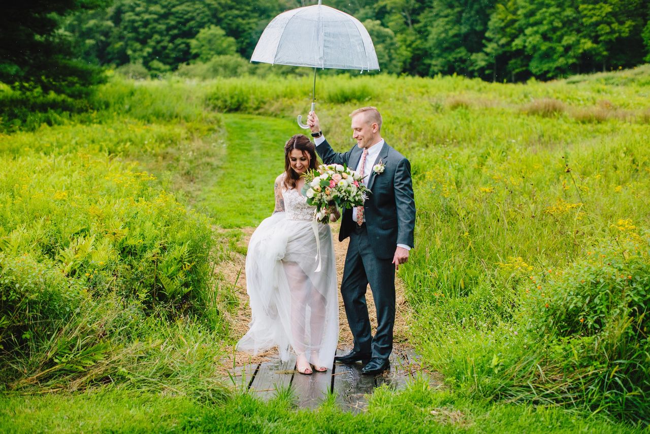 Bride and Groom on grass, groom holding umbrella over Bride
