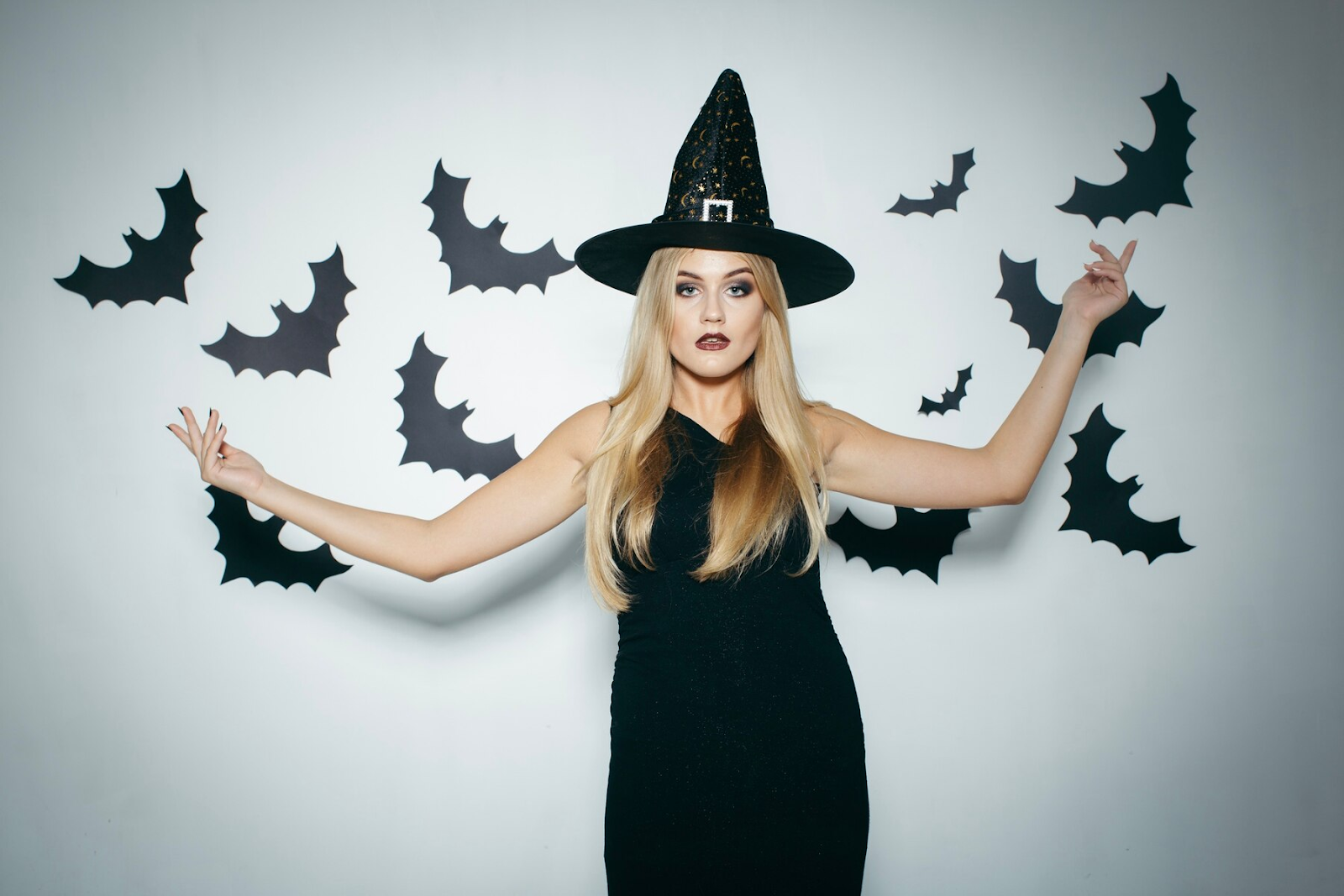 A woman wearing a witch hat with bats around her.