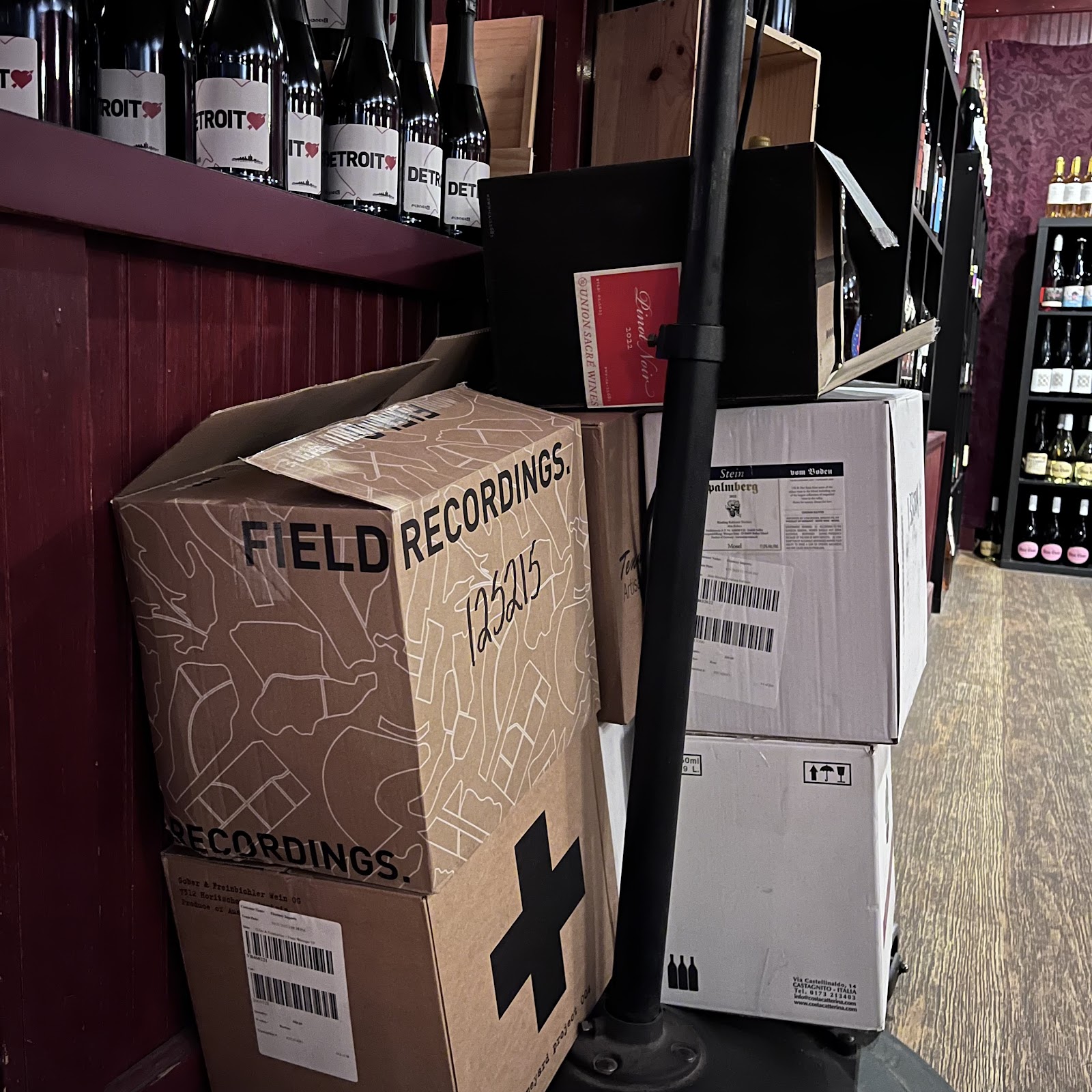 Picture of boxes on the floor in a wine shop with shelves full of wine. One of the boxes says, "FIELD RECORDINGS".