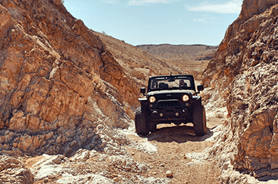 A jeep driving through a rocky canyon                                                                            Description automatically generated
