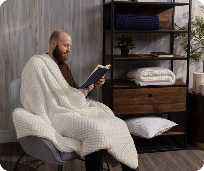 Our White Bamboo Cotton Waffle Blanket shown draped on a man reading a book in a room.