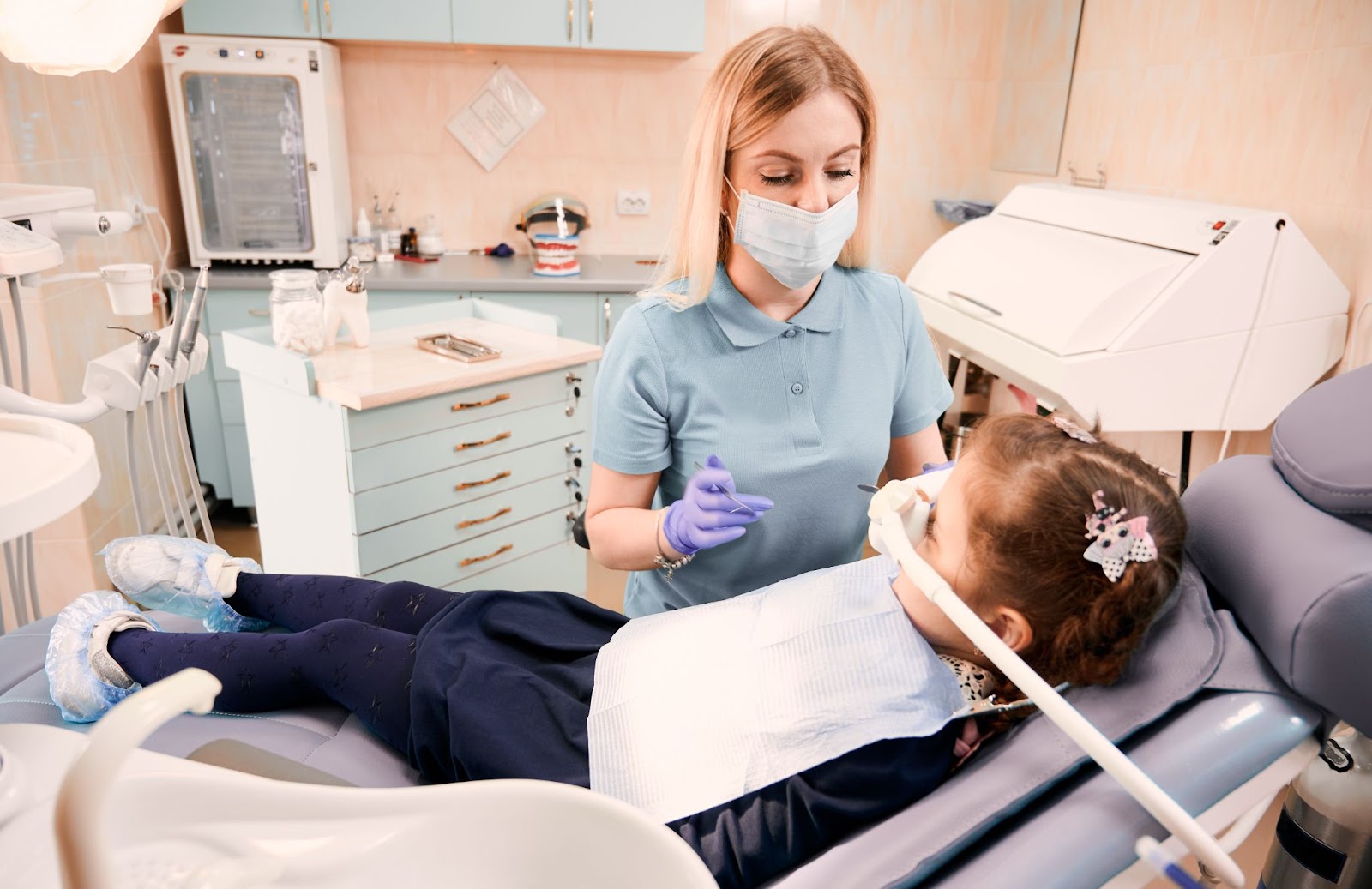 Little girl undergoing dental treatment with nitrous oxide and dentist looking at little girl