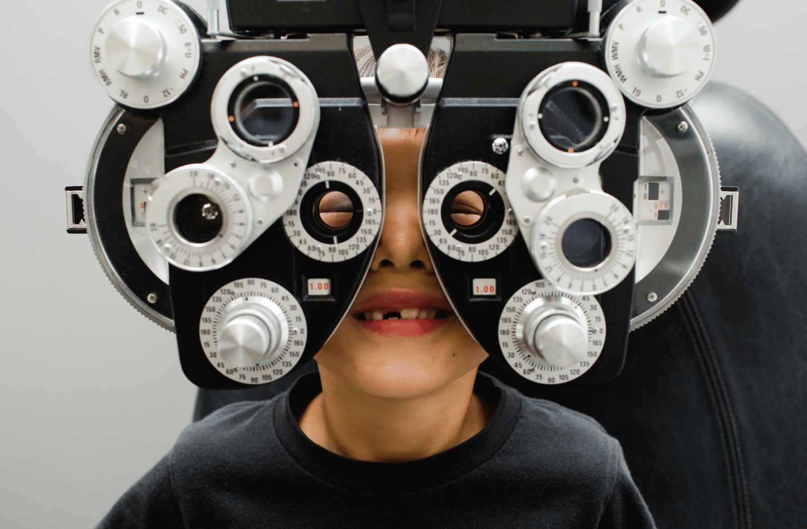 A young boy sits behind a phoropter at the optometrists office